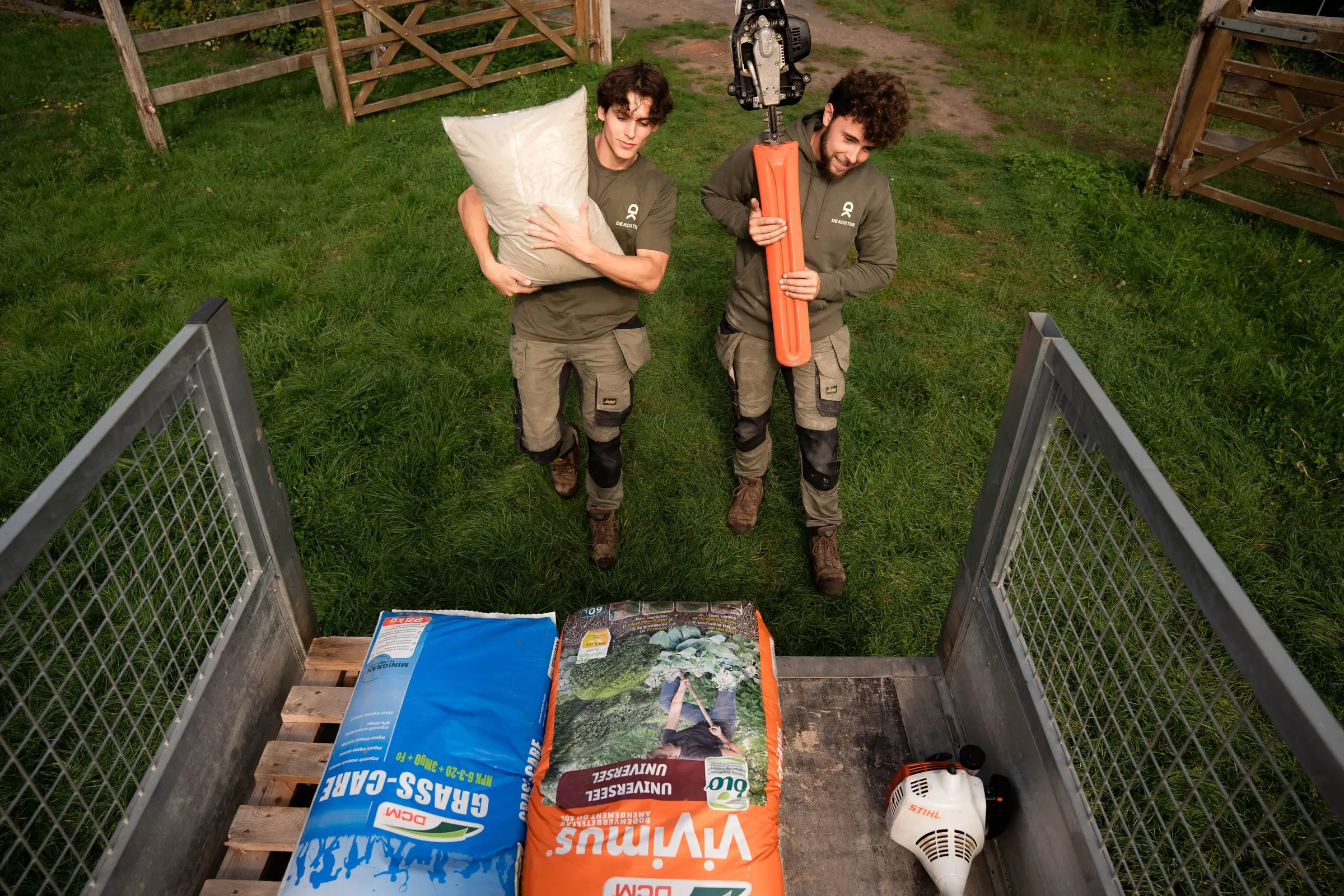 Twee collega's staan klaar met een zak potgrond en een heggenschaar