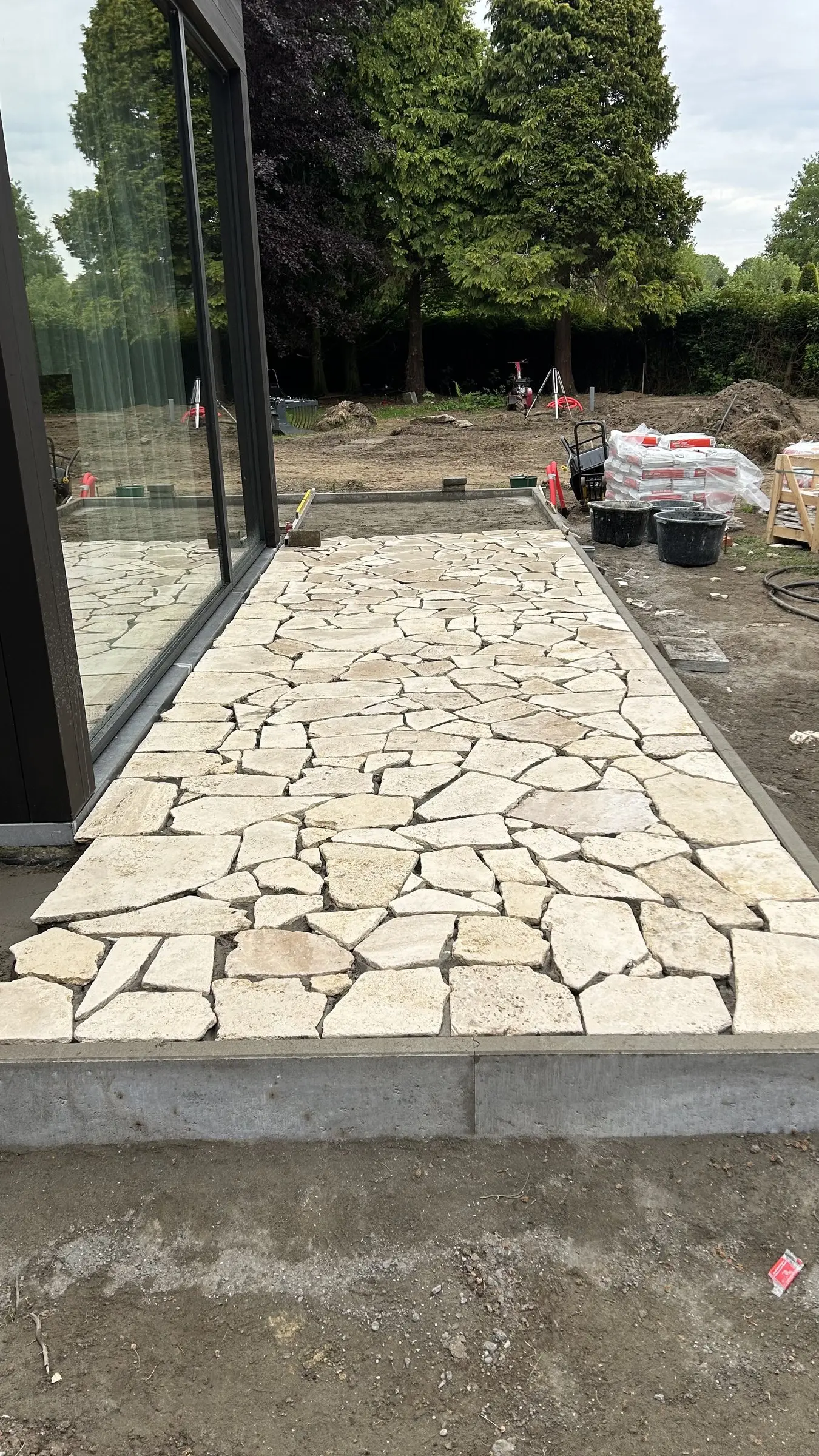 Natuursteen terras in aanleg langs de glazen gevel